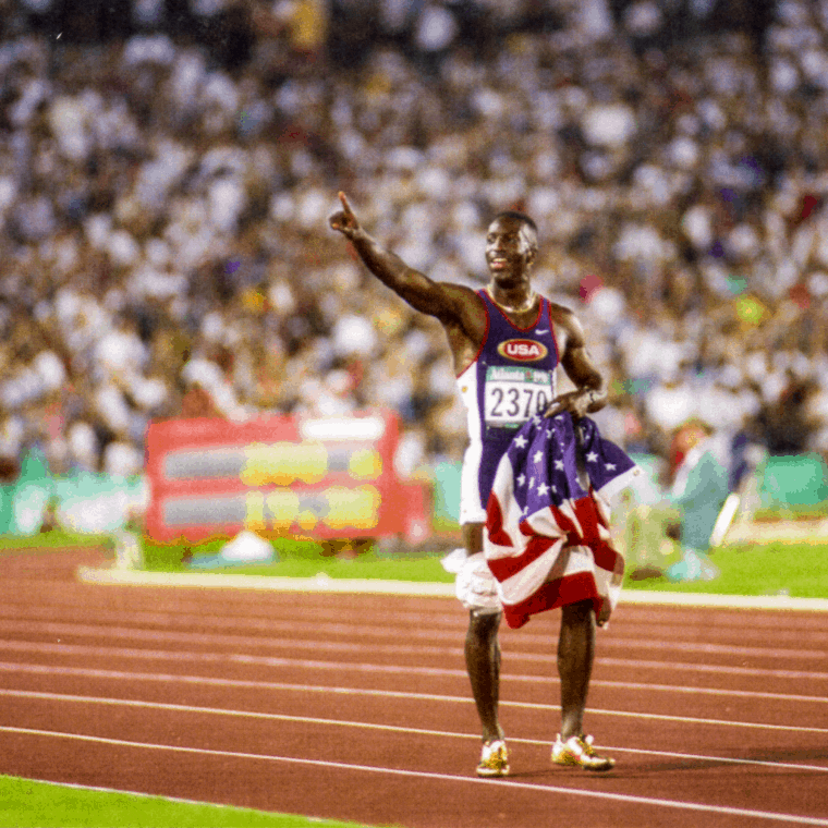 Image of Black track runner holding American flag and pointing while standing on track