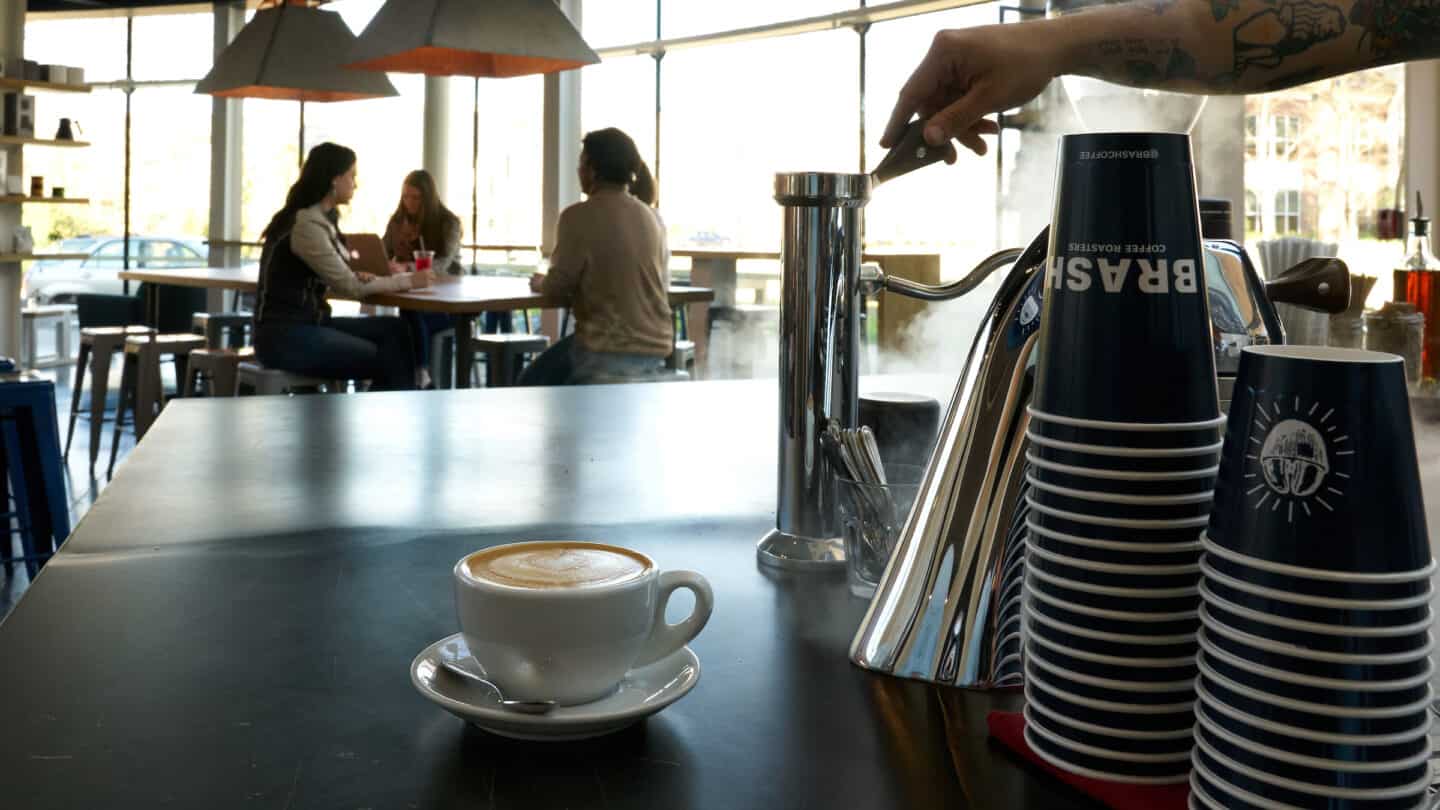 view of a cappuccino and three guests sitting at the table, one with a laptop