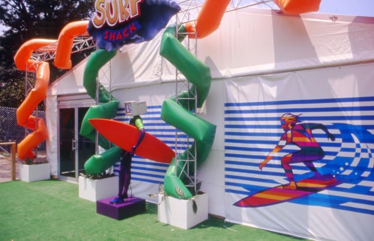 Exterior of a tent labeled Surf Shack with a statue of a surfer in front