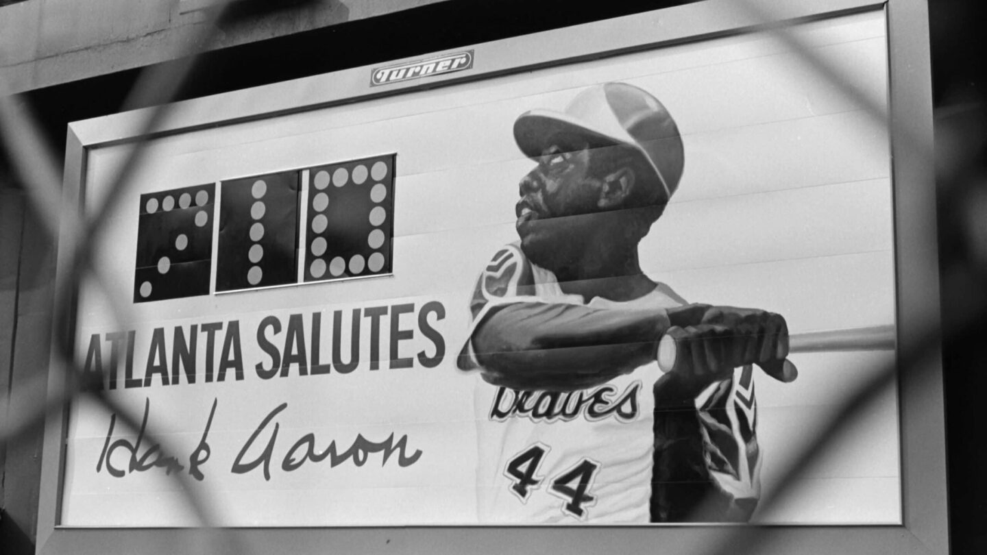 White billboard with black writing (Atlanta Salutes Hank Aaron), a painting of Hank Aaron and a scoreboard reading 710
