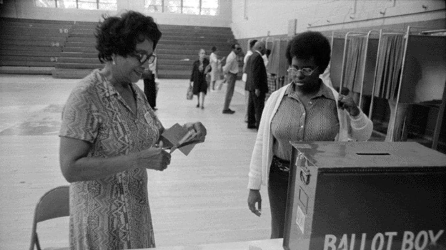 Black and white image of two females in front of a ballot box in Fulton County