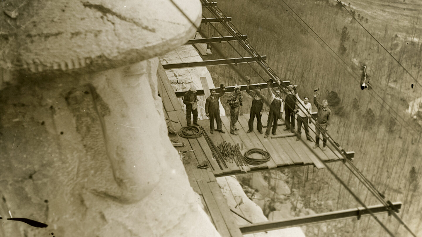 Workers stand on a scaffolding beside Robert E. Lee's carved face and hat, 1928.