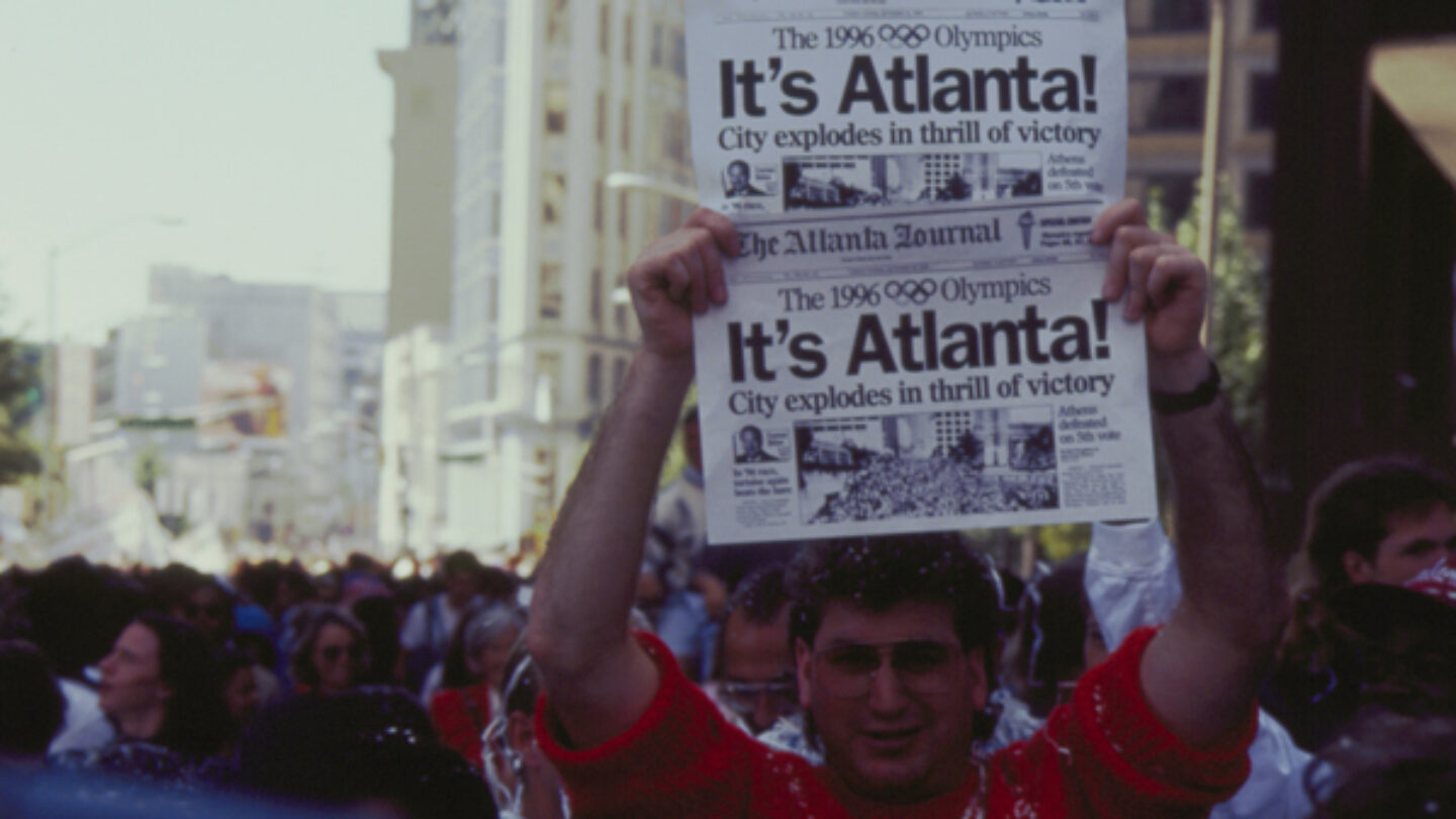 A man holds up copies of the Atlanta Journal announcing Atlanta's selection to host the 1996 Olympic Games, September 1990.