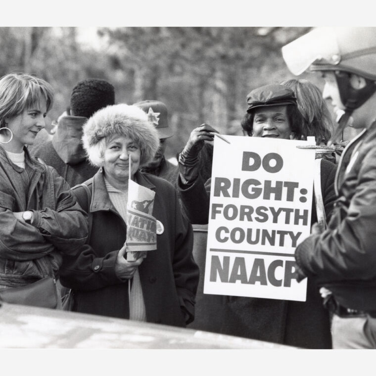 Protestors with signs stand near a member of the Georgia State Patrol at the second Brotherhood March. Members of the Georgia State Patrol were at the march to ensure the safety of protestors