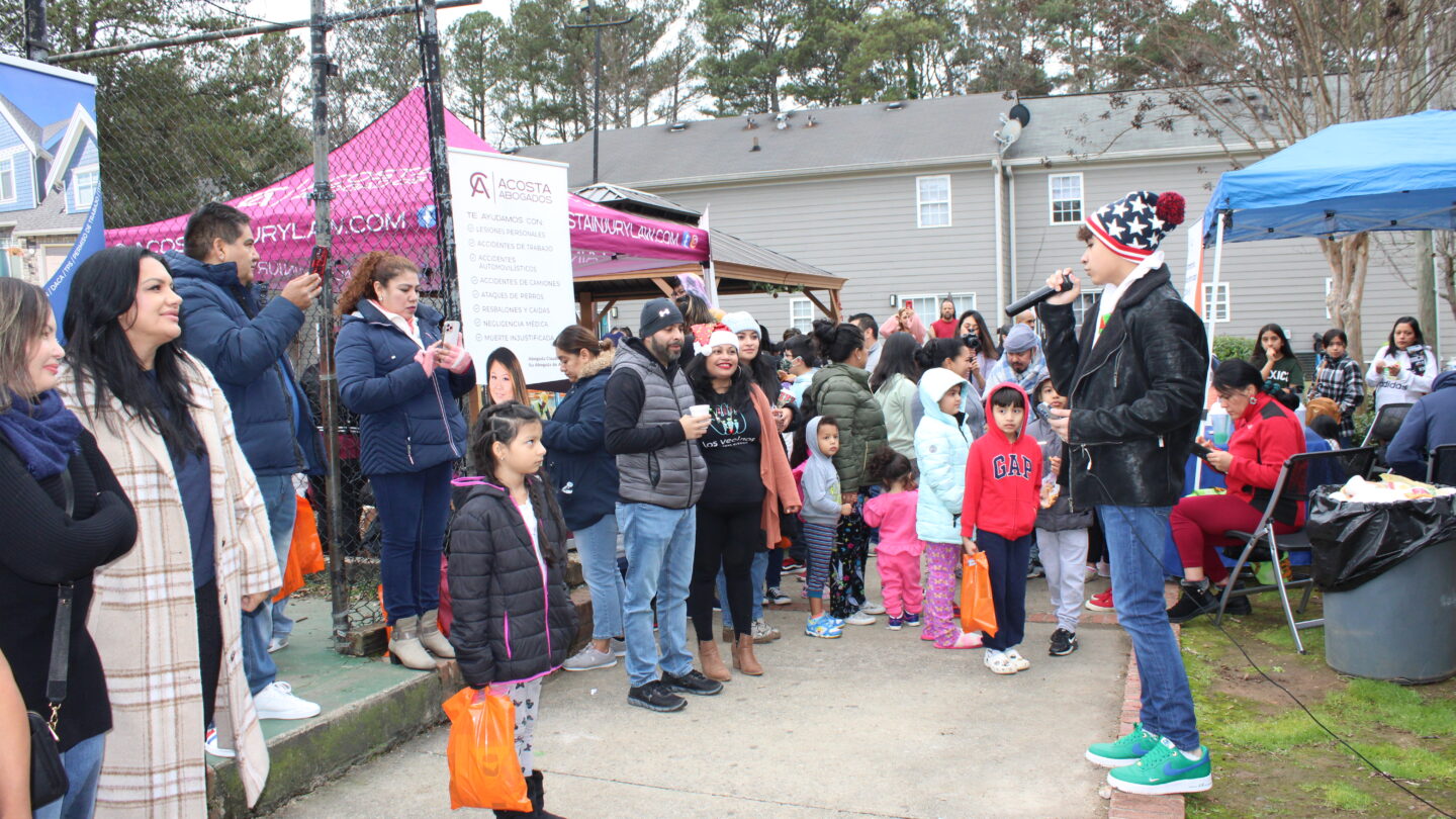 Residents, volunteers, and organizers with Los Vecinos gather to hear local musician Henry Torres sing at the Los Vecinos de Buford Highway Christmas party