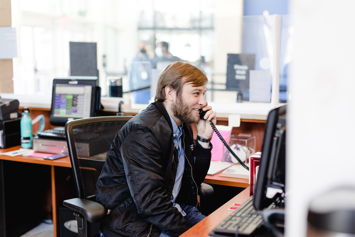 Guest experience ambassador sitting at admission desk on phone.